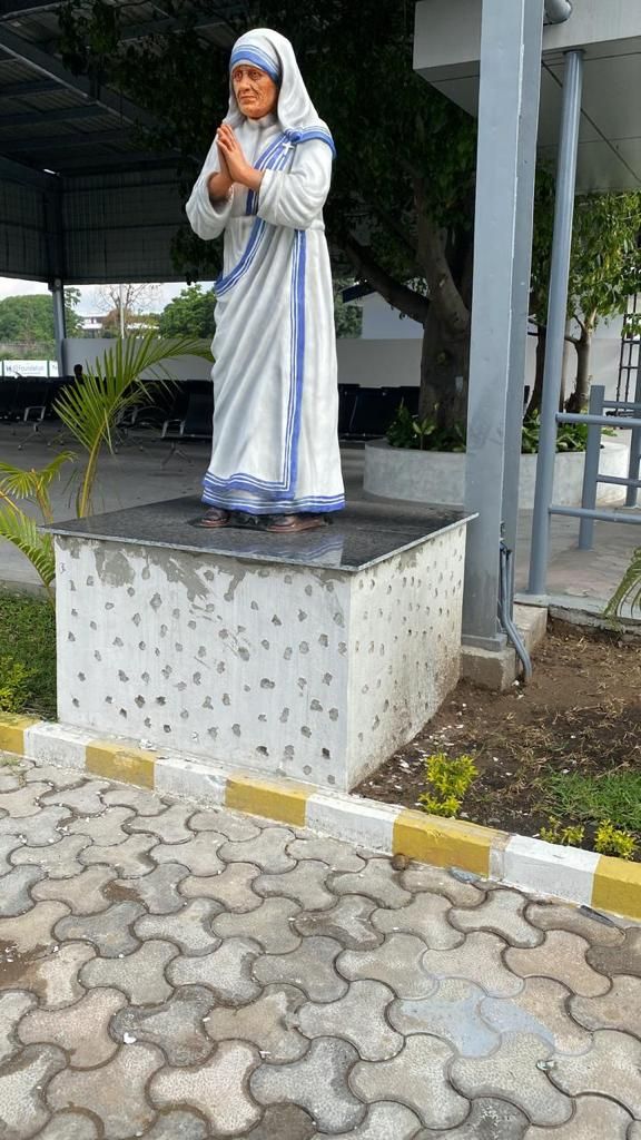 Painted statue of Mother Teresa, hands joined, in a white sari with blue borders