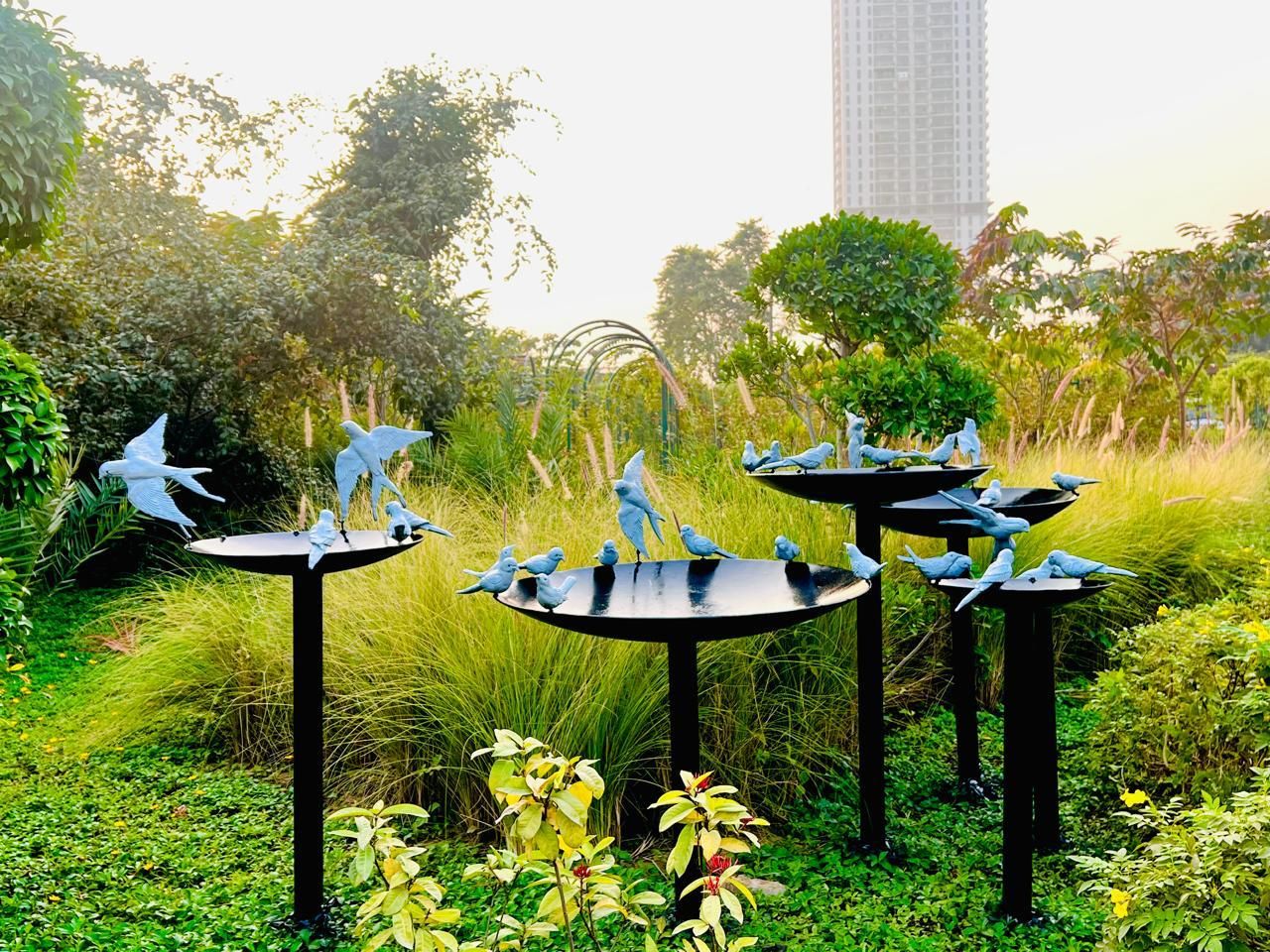 Silver bird sculptures perched on dark bird-bath stands among tall grasses