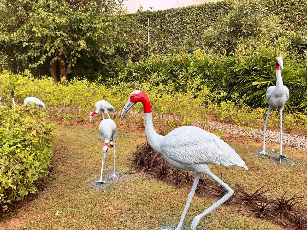 White crane sculptures with red crowns standing among garden planting