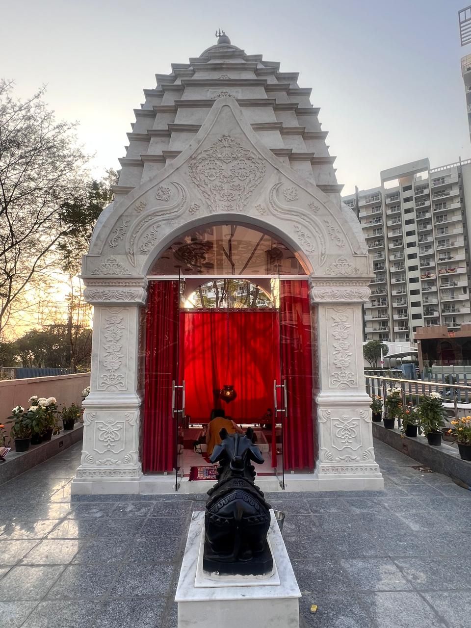 Front view of the temple: carved marble arch and pillars, red curtains within, Nandi in the foreground