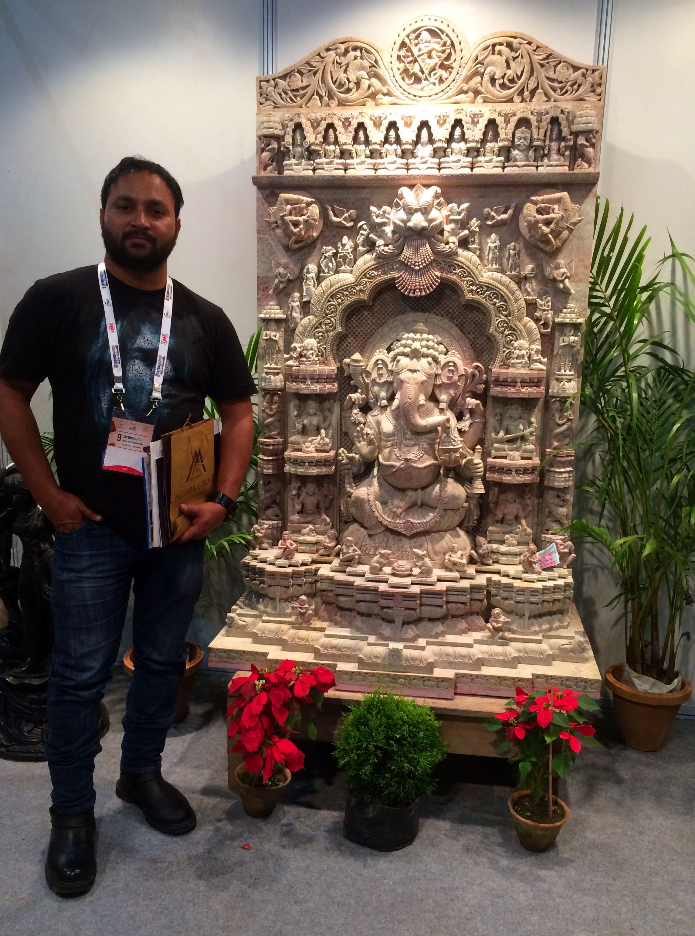 Pawan Kumar Bhatt standing beside a carved sandstone Ganesha shrine at an exhibition