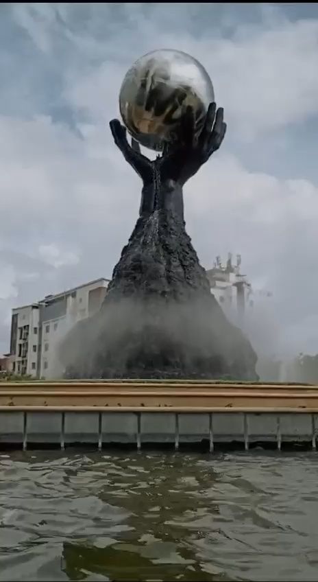Sculpted hands rising from a rock mound holding a mirror-steel globe in a fountain