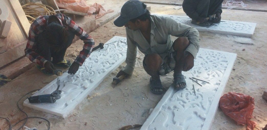 Two artisans hand-carving white marble relief panels