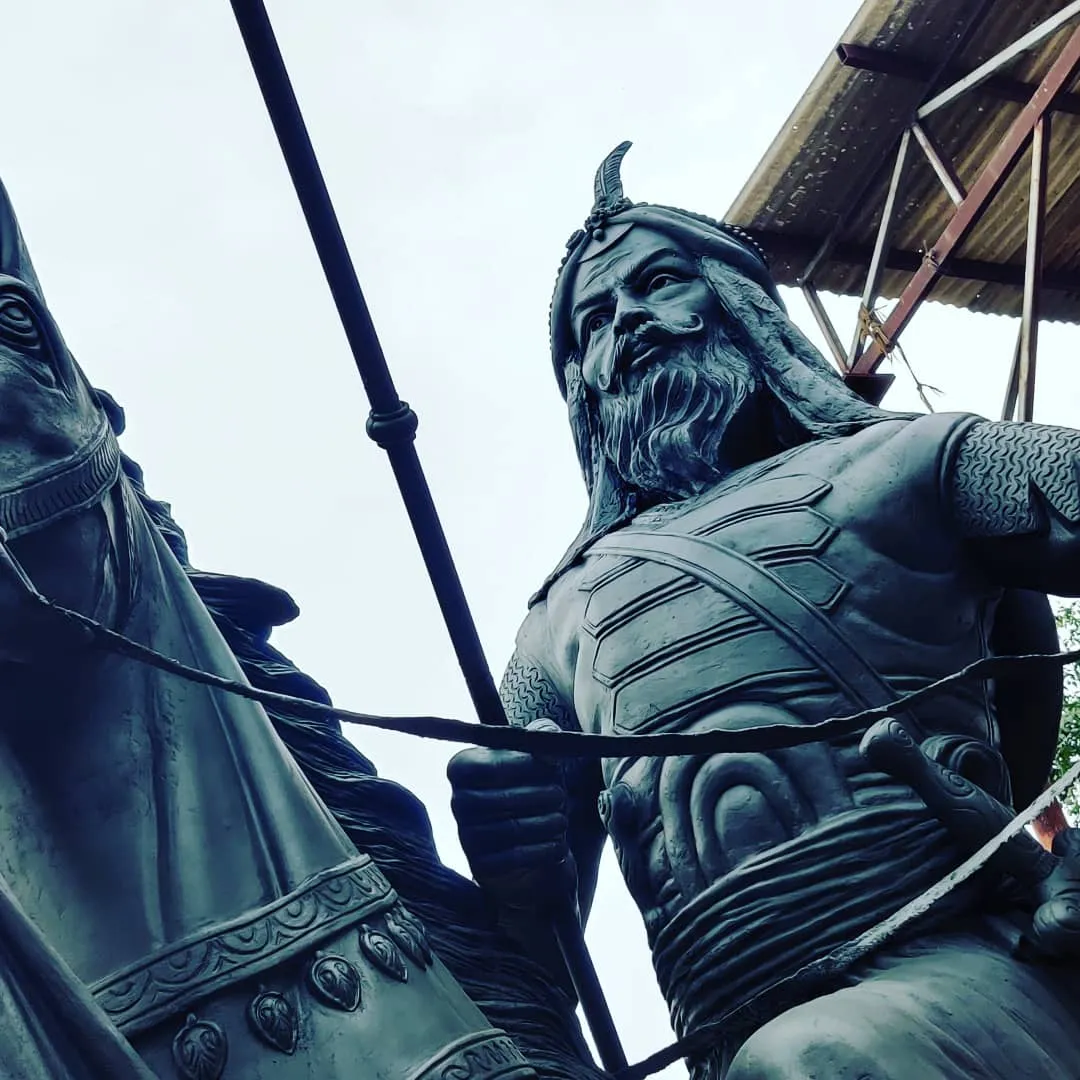 Detail of a dark metal warrior figure with a spear, seen from below
