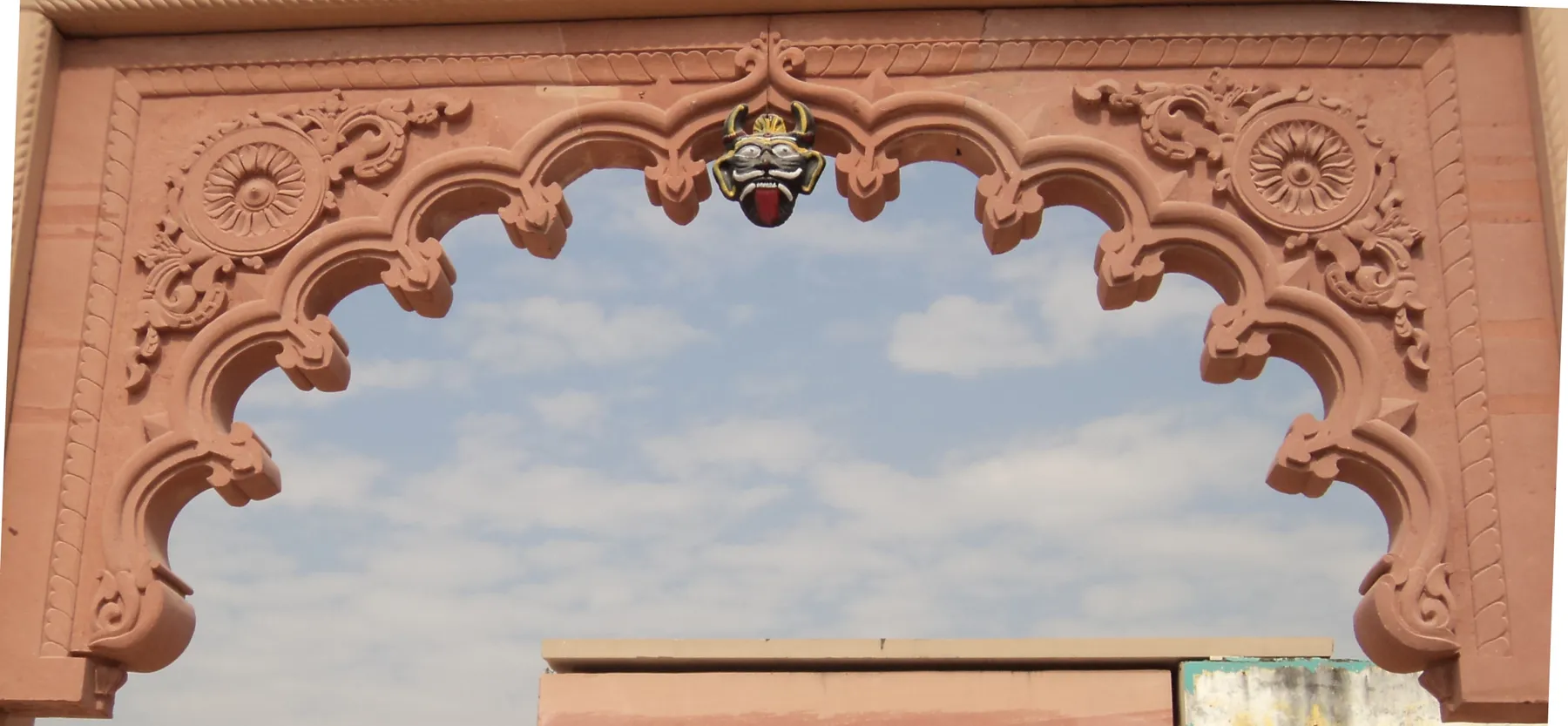 A carved sandstone arch with a scalloped opening, against the sky