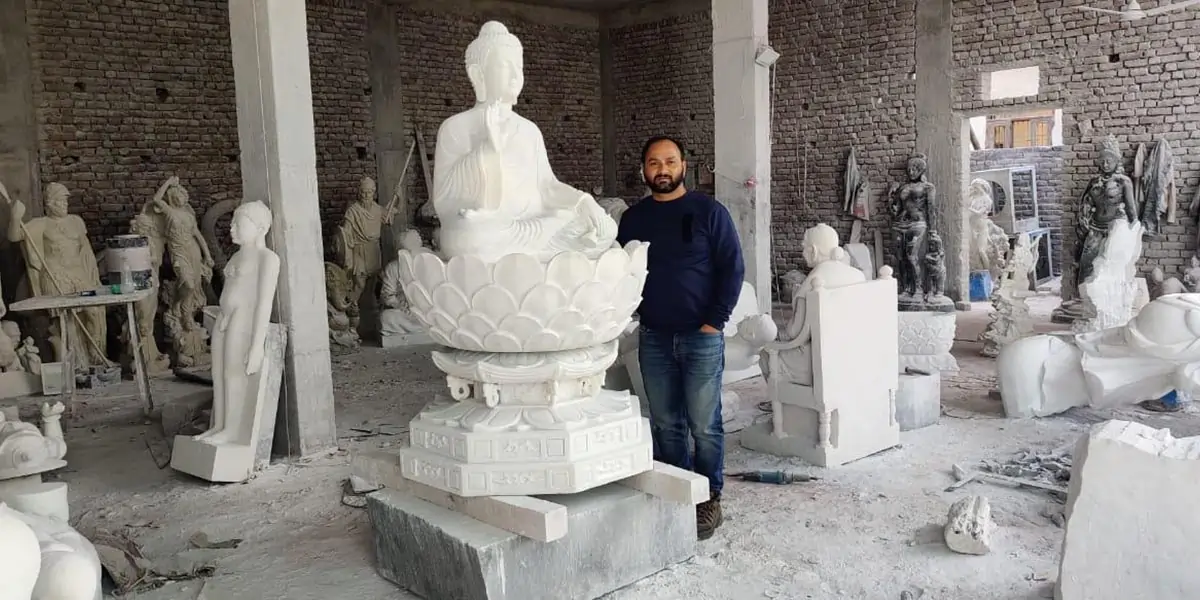 A white marble seated Buddha on a lotus base in the studio workshop, with its sculptor